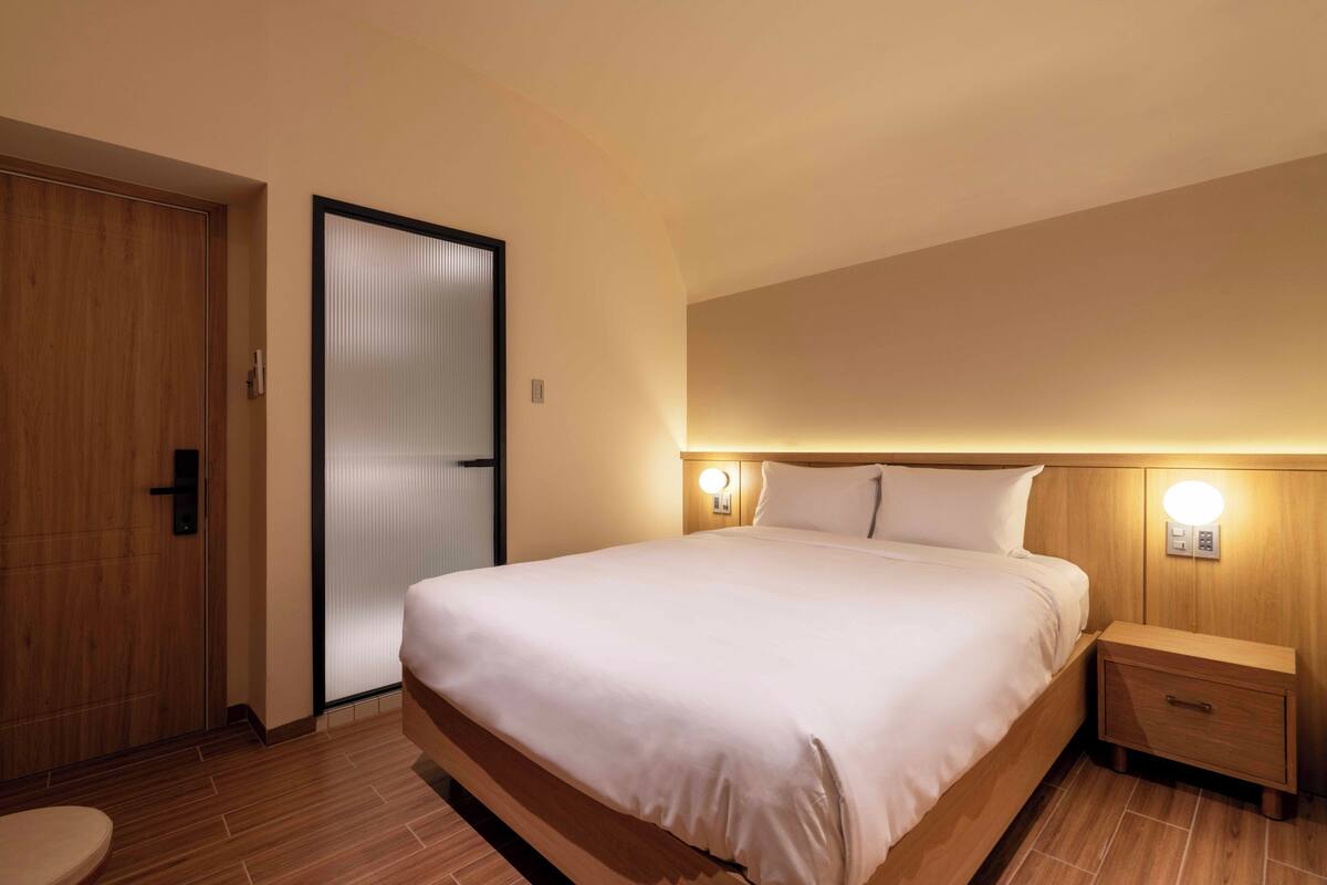 Une chambre d’hôtel avec un grand lit, des tables de chevet, une porte en bois et un luminaire fixé au mur.