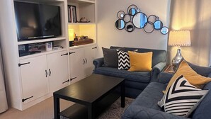 Una sala de estar con un sofá gris, una mesa de centro negra y un mueble blanco para el televisor.
