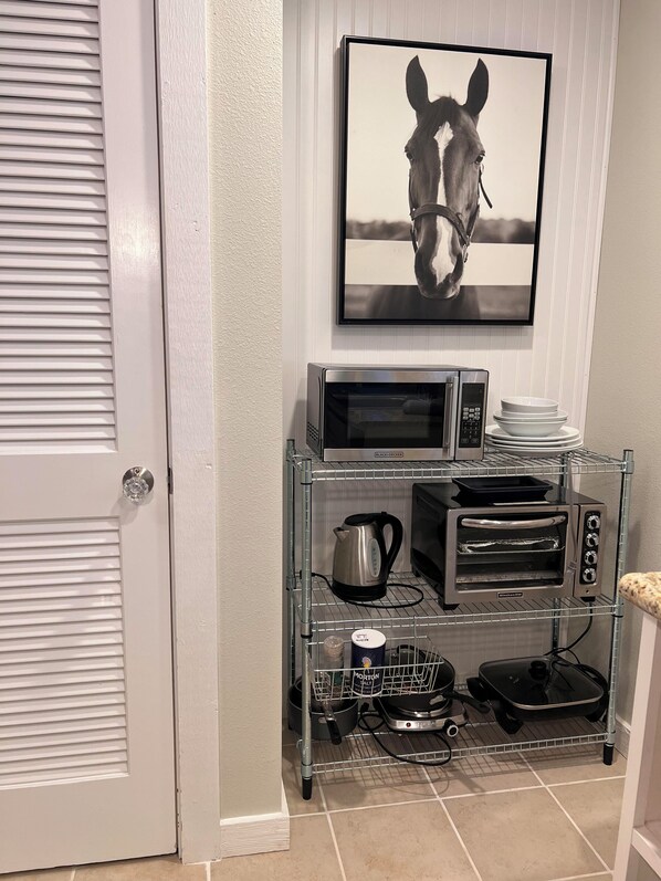 A kitchen with a microwave, toaster oven, kettle, and a coffee maker on a metal shelf.