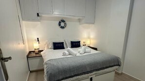 Een slaapkamer met een bed, nachtkastjes, een plafondlamp en een aan de muur bevestigde reddingsboei.