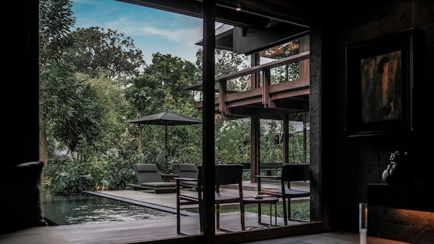A modern interior with a large glass window overlooking a lush garden and a pool. - Janjisurga by Ekosistem (Cepaka)