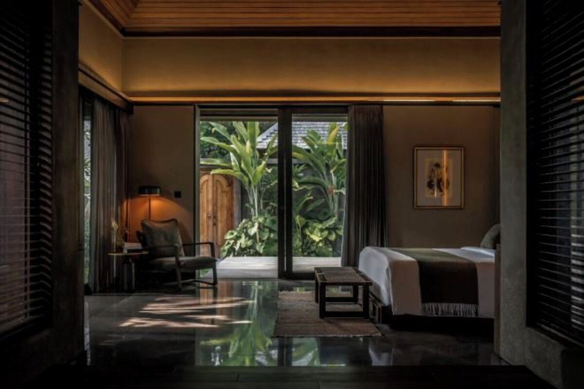 A modern bedroom with a large sliding glass door leading to a garden, a bed, a bedside table, and a chair.