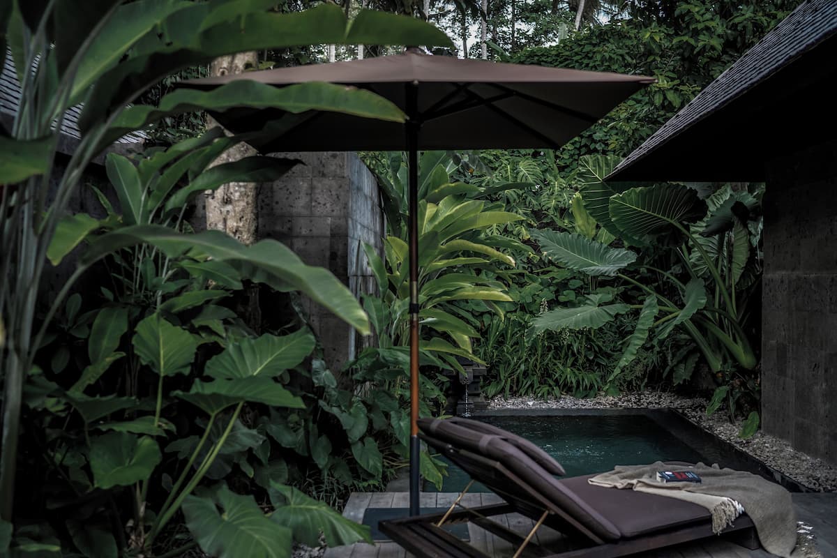 Ein privater Poolbereich mit Liegestuhl und Sonnenschirm, umgeben von üppiger tropischer Vegetation.
