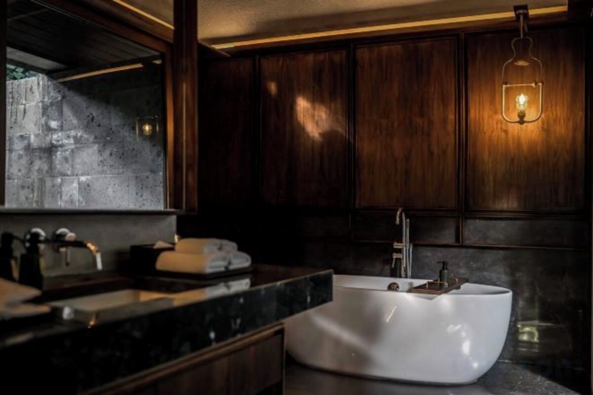 A modern bathroom with a freestanding bathtub, dark wood cabinetry, and a mirror with a light fixture above it.