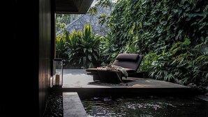A serene outdoor seating area with a pool, surrounded by lush greenery and a view of a traditional roofed structure in the background. - Janjisurga by Ekosistem (Cepaka)