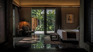 A modern bedroom with a large sliding glass door leading to a garden, a bed, a bedside table, and a chair. - Janjisurga by Ekosistem (Cepaka)