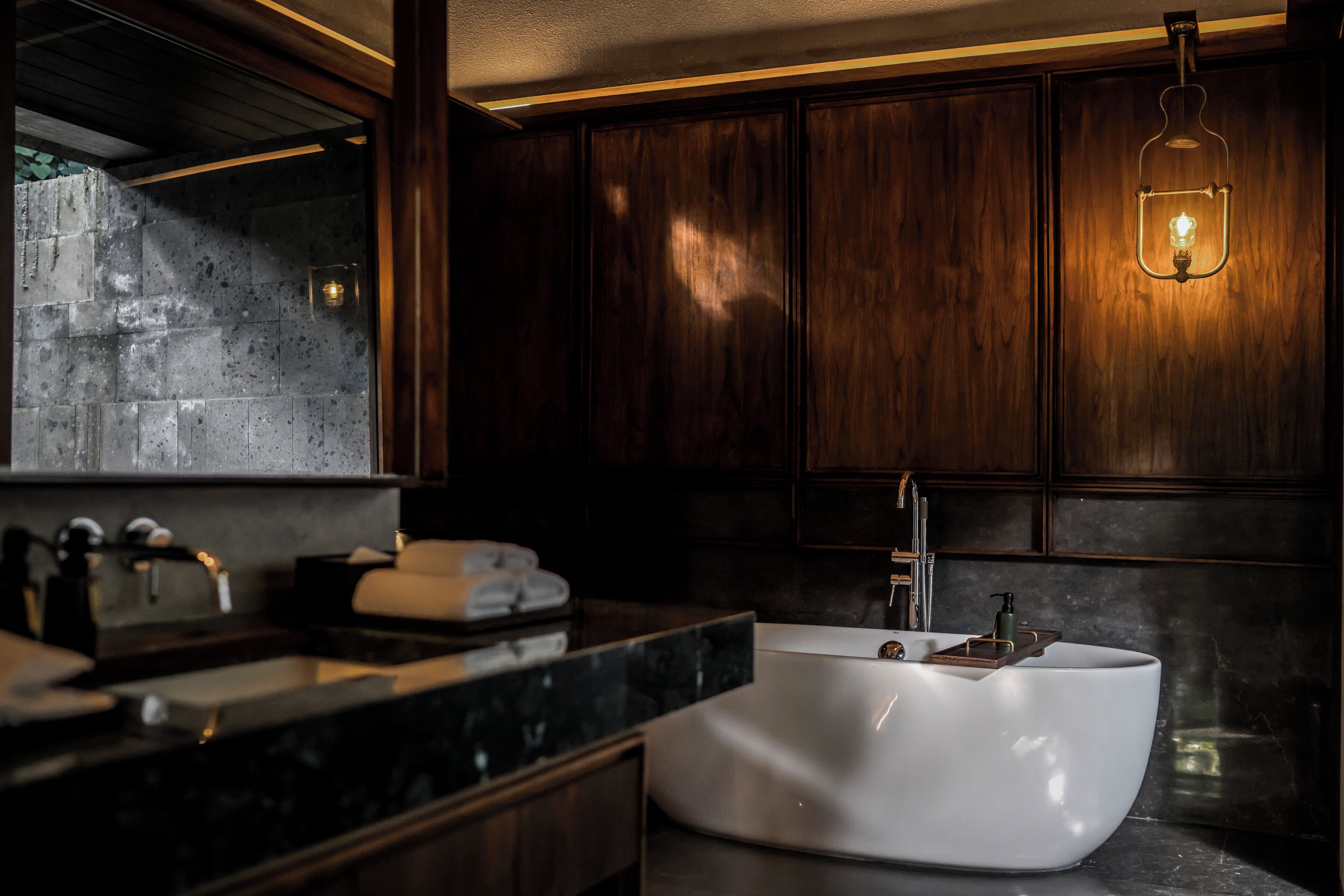 A modern bathroom with a freestanding bathtub, dark wood cabinetry, and a marble countertop.