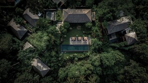 An aerial view of a resort with multiple geometric-roofed buildings, a central swimming pool, and lush greenery surrounding the area. - Janjisurga by Ekosistem (Cepaka)