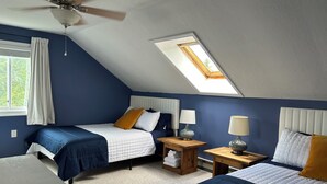 A bedroom with two beds, a ceiling fan, a skylight, and a small wooden nightstand with a lamp.