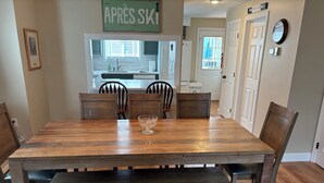 A dining area with a wooden table and chairs, a small glass bowl, and a sign above the table reading "APRES SKI".