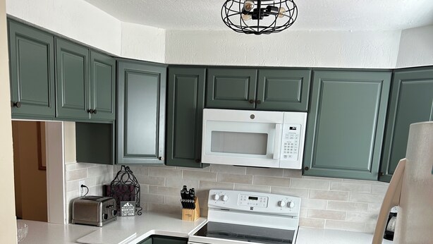 A kitchen with green cabinets, a white microwave, a stove, and a toaster.