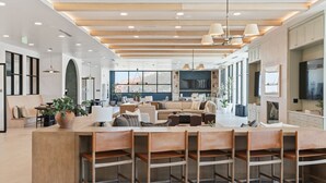 A modern hotel lobby with a central seating area, a bar, and a large TV screen.
