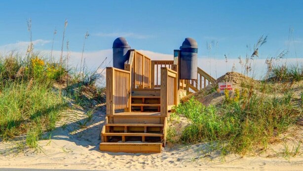 Een houten trap naar het strand, leidend naar een duingebied met een bord waarop staat 'Blijf van de duin af'.