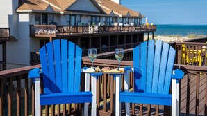 Een terras met twee blauwe Adirondack-stoelen, een tafeltje met een glas witte wijn en een dienblad met eten.