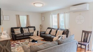 A living room with two sofas, a coffee table, and a chair. There is a TV on a stand, a decorative wall piece, and an air conditioning unit. - Harbor ViewCharming 3-bedroom house in delightful Acadia Area AC, WiFi (Ellsworth)