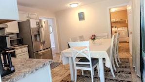 A compact kitchen with a refrigerator, microwave, and coffee maker. A dining table with chairs is set in the center, and a patterned rug covers the floor. - Harbor ViewCharming 3-bedroom house in delightful Acadia Area AC, WiFi (Ellsworth)