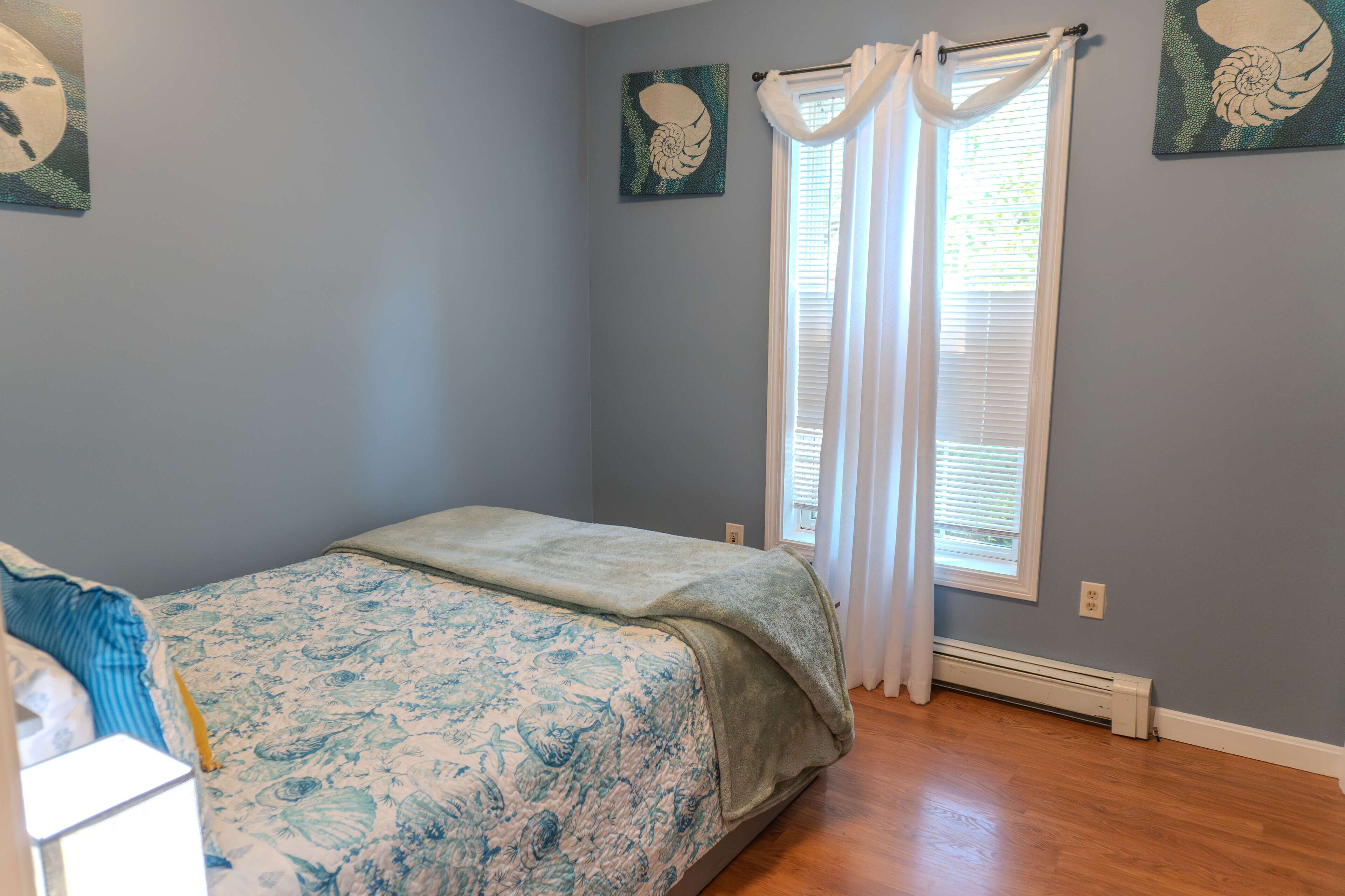 A bedroom with a bed, a window with curtains, and wall art.