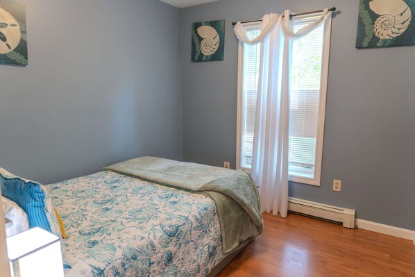 A bedroom with a bed, a window with curtains, and wall art.