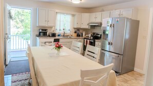 A kitchen with white cabinets, a stainless steel refrigerator, and a dining table with chairs. - Harbor ViewCharming 3-bedroom house in delightful Acadia Area AC, WiFi (Ellsworth)