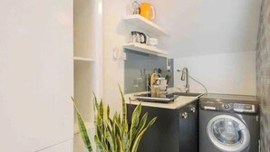 Een kleine wasruimte met een wasmachine, een wastafel en een klein plankje met keukenspullen.