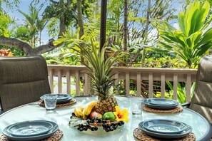 A round glass table set outdoors with plates, glasses, and a fruit centerpiece.
