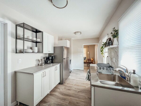 Una cocina moderna con armarios blancos, un refrigerador de acero inoxidable y una cafetera.