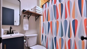 Ein Badezimmer mit Toilette, Waschbecken und Spiegel. Ein Handtuchhalter mit Handtüchern und eine Duschkabine mit geometrischem Muster.