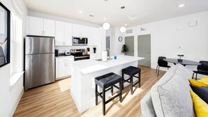 A modern kitchen with white cabinetry, a stainless steel refrigerator, a microwave, and a central island with stools.