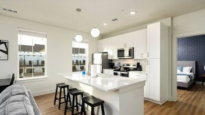 Una cocina moderna con armarios blancos, una isla central con taburetes, un microondas y un refrigerador.