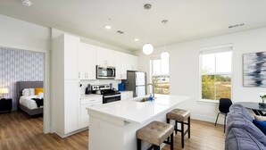 A modern kitchen with white cabinetry, a central island, and a dining area with a view. - Refined Living in a Vibrant Locale – Dream Stay (Pflugerville)