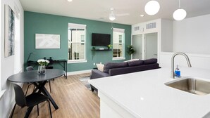 A modern living room with a sofa, a dining table with chairs, and a kitchen area with a sink and a ceiling fan. - Refined Living in a Vibrant Locale – Dream Stay (Pflugerville)