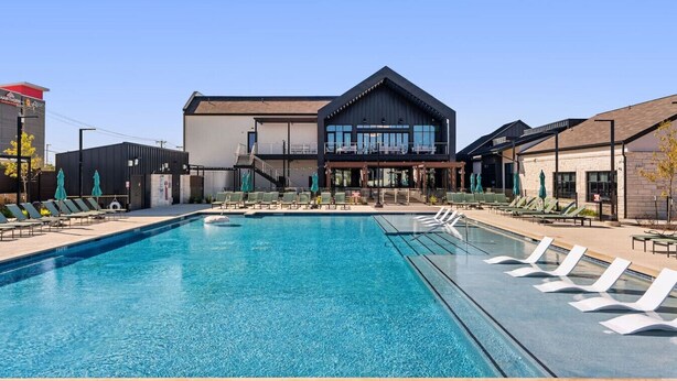 A swimming pool with lounge chairs and umbrellas, a building with a modern design, and a clear blue sky. - Perfect Environment w toptier furnishing/amenities (Pflugerville)