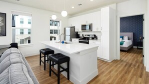 A modern kitchen with white cabinetry, a central island with stools, a microwave, and a refrigerator. - Perfect Environment w toptier furnishing/amenities (Pflugerville)
