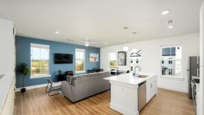 A modern kitchen with white cabinetry, a central island, and a dining area with a gray sofa. - Perfect Environment w toptier furnishing/amenities (Pflugerville)