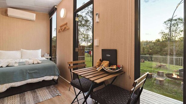Ein Schlafzimmer mit einem Bett, einem Holztisch mit Stühlen und Blick ins Freie.