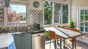 Een moderne keuken met een vaatwasser, een eethoek met tafel en stoelen, en grote ramen met uitzicht op bomen en heuvels.
