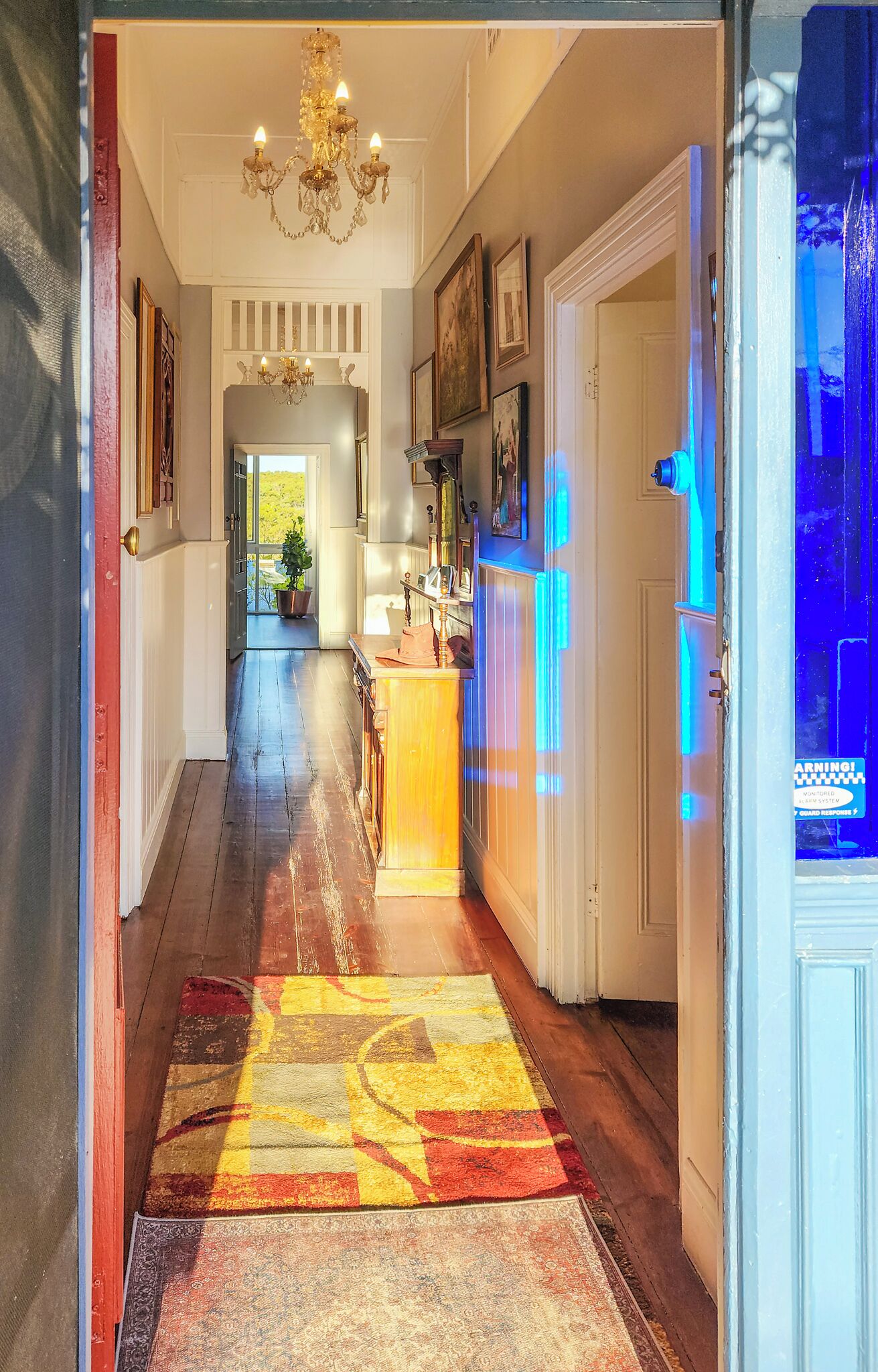 Um corredor com um candelabro, um tapete estampado e uma porta com luz azul.