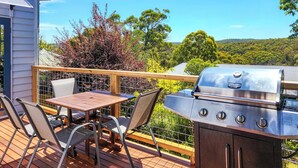 Een terras buiten met een barbecue, een tafel en stoelen.