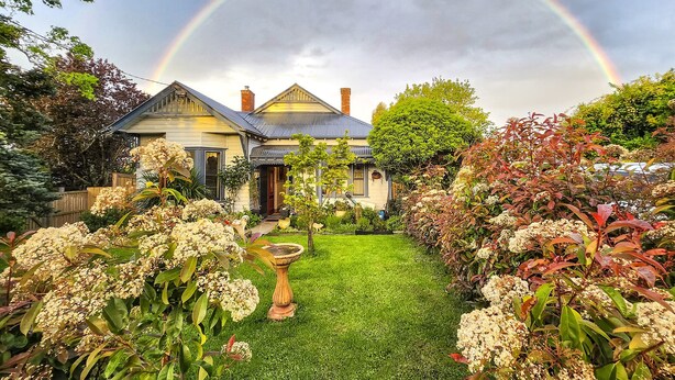 Een huis met een tuin, een vogelbad en een regenboog aan de lucht.
