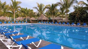 A swimming pool with blue lounge chairs and thatched umbrellas.