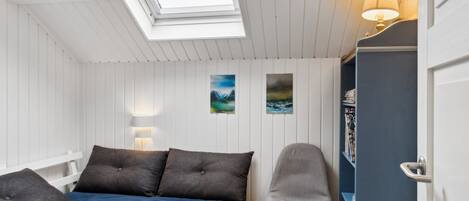 A bedroom with a skylight, a bed with dark bedding, a chair, and a bookshelf.