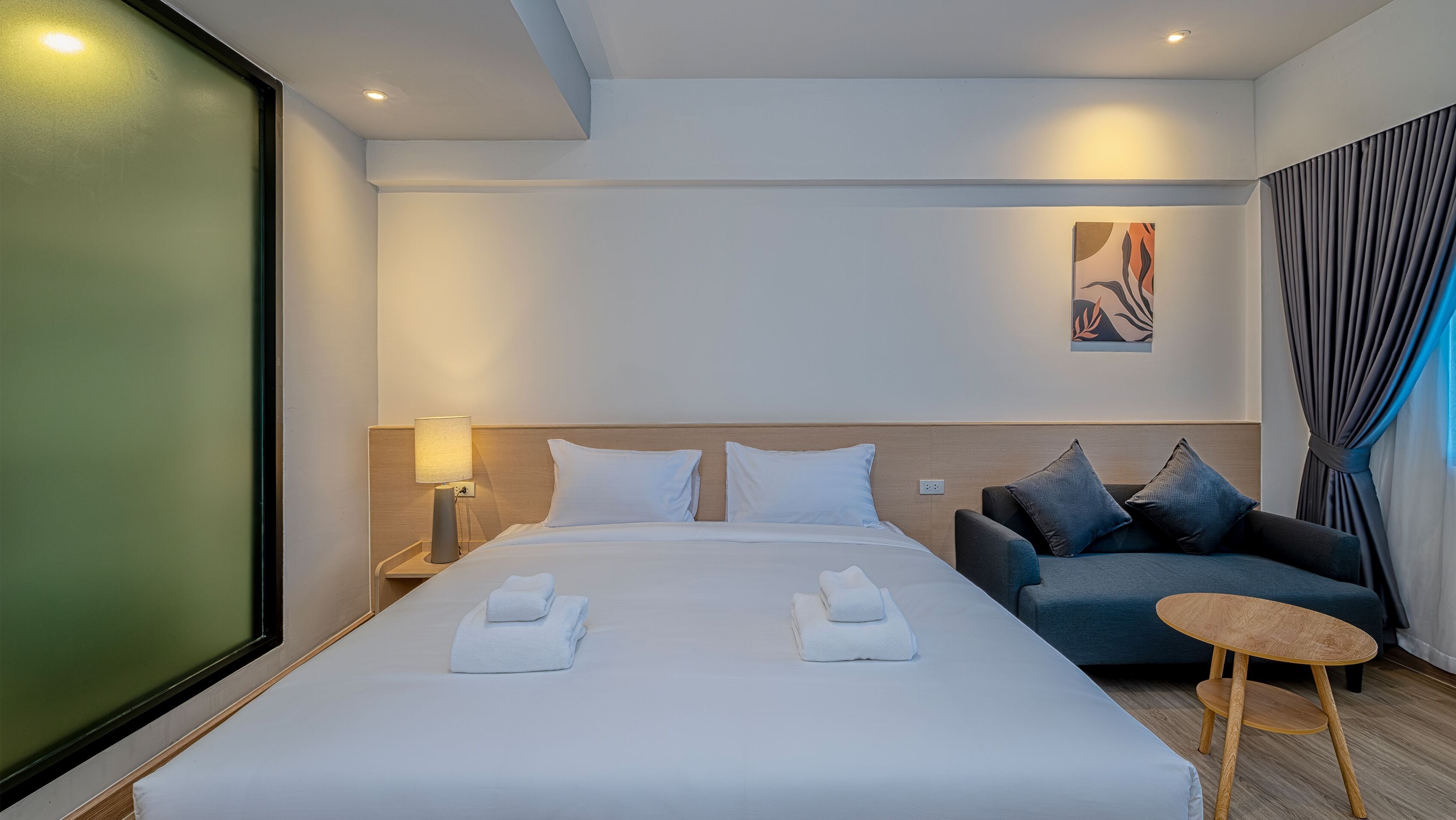 A hotel room with a large bed, a bedside table with a lamp, a sofa, and a small round table.