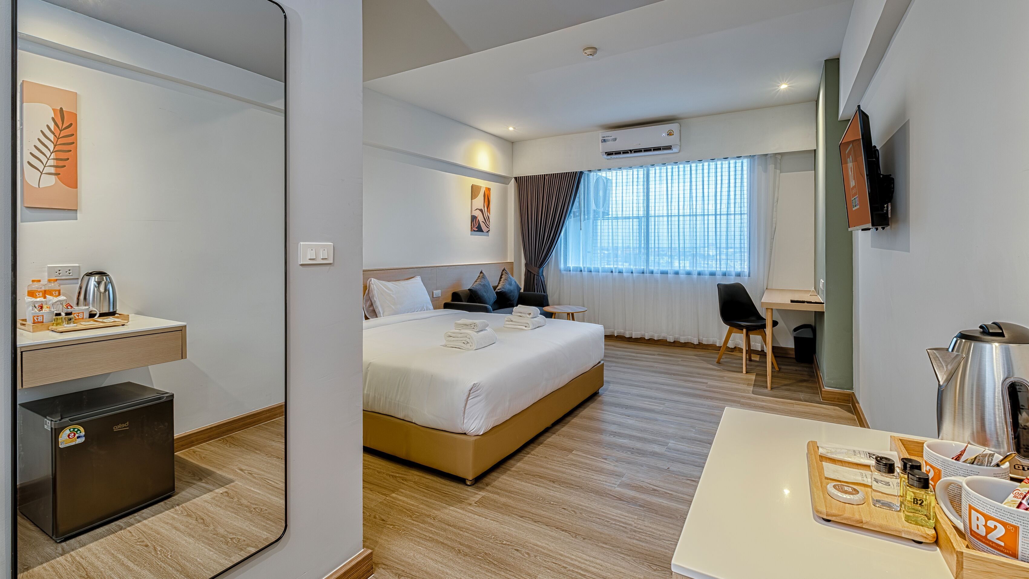 A hotel room with a bed, bedside table, desk, chair, and a minibar.