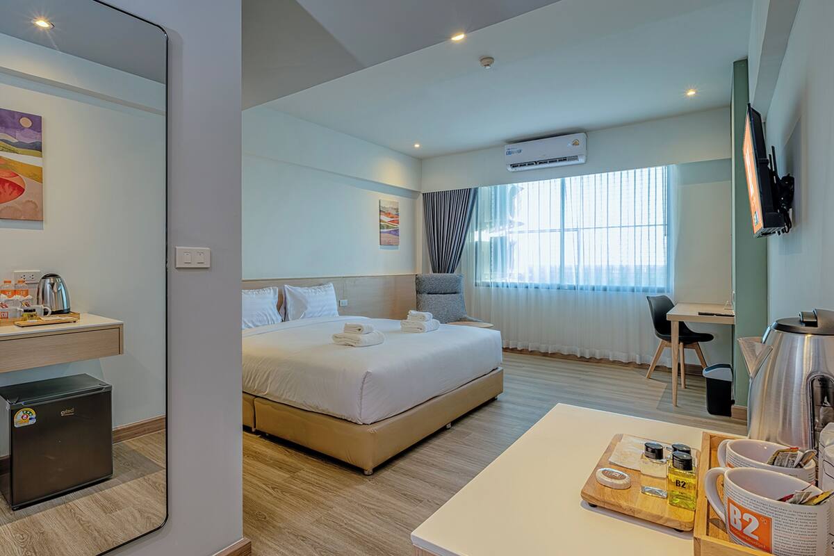 A hotel room with a bed, a desk, a chair, a coffee maker, a mini fridge, and a TV.