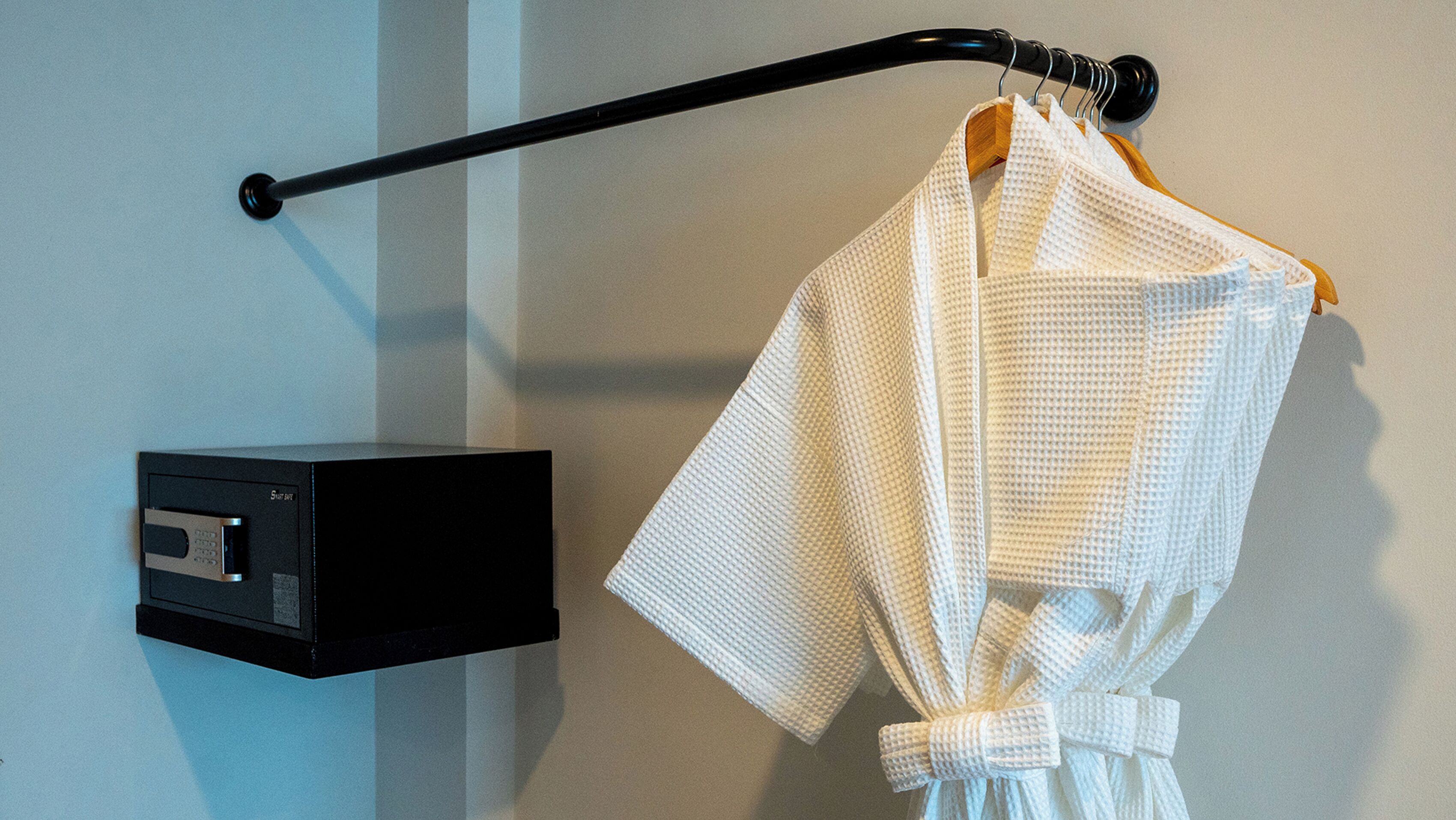 A white robe hanging on a black towel rack against a light-colored wall.
