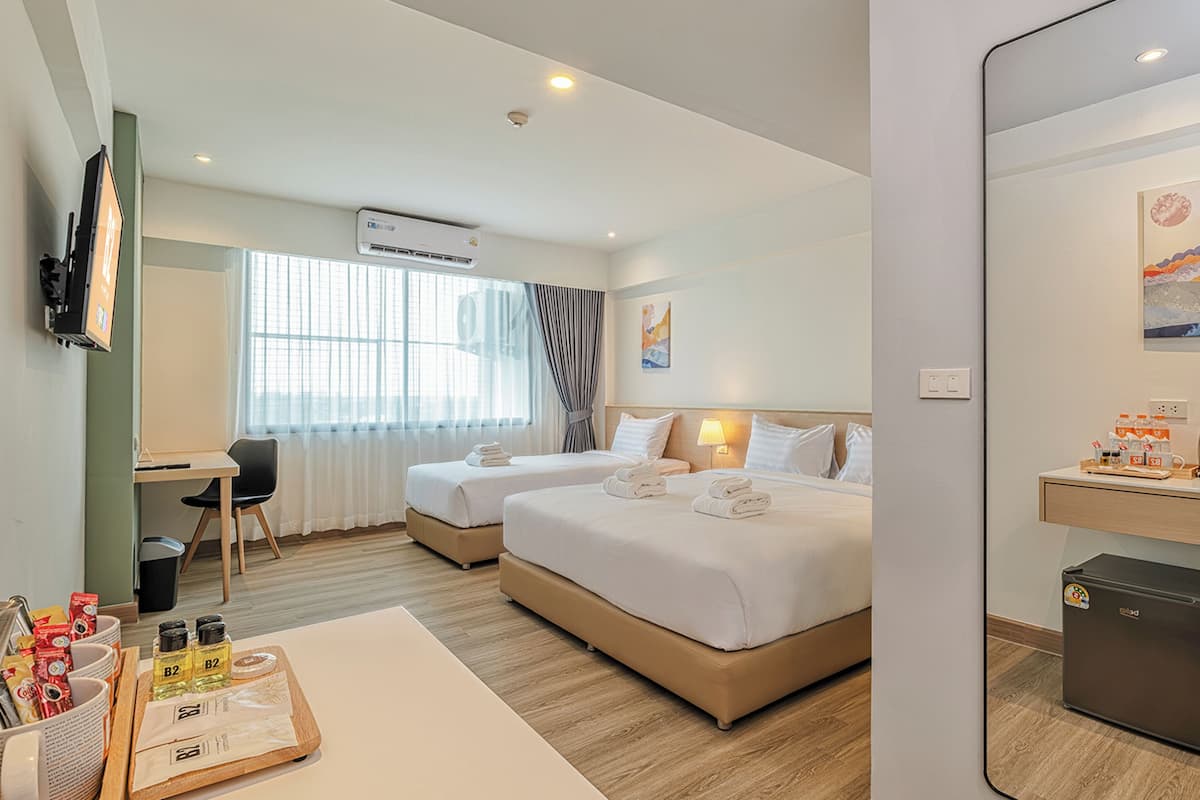 A hotel room with two beds, a desk, a chair, a small refrigerator, and a TV mounted on the wall.