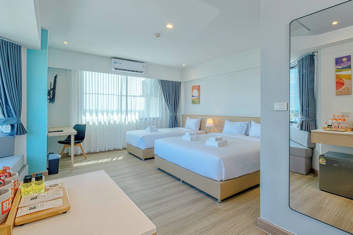 A hotel room with two beds, a desk, a chair, a small kitchenette, and a bathroom.