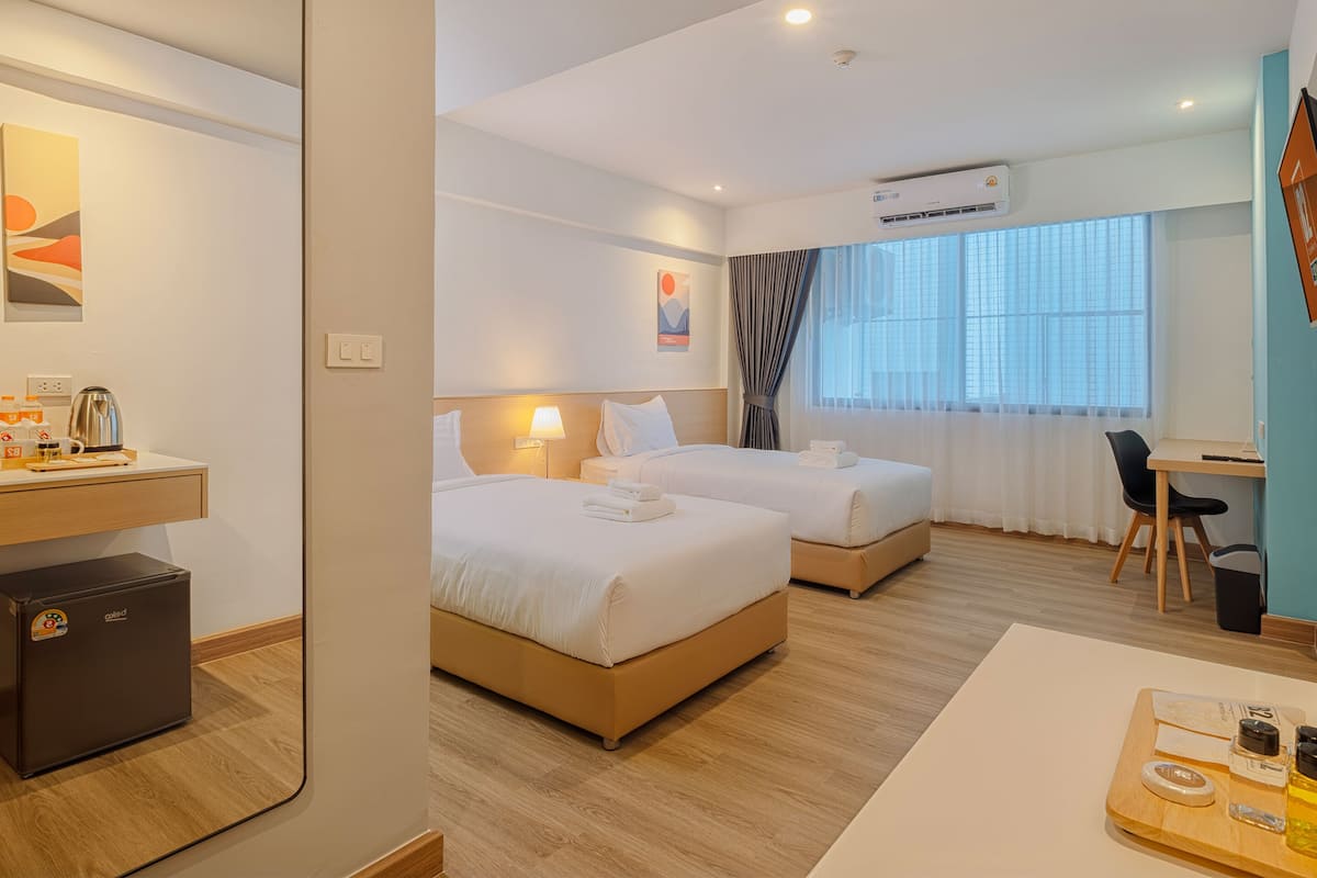 A hotel room with two beds, a desk, a chair, a coffee machine, a mini-fridge, and a TV on the wall.