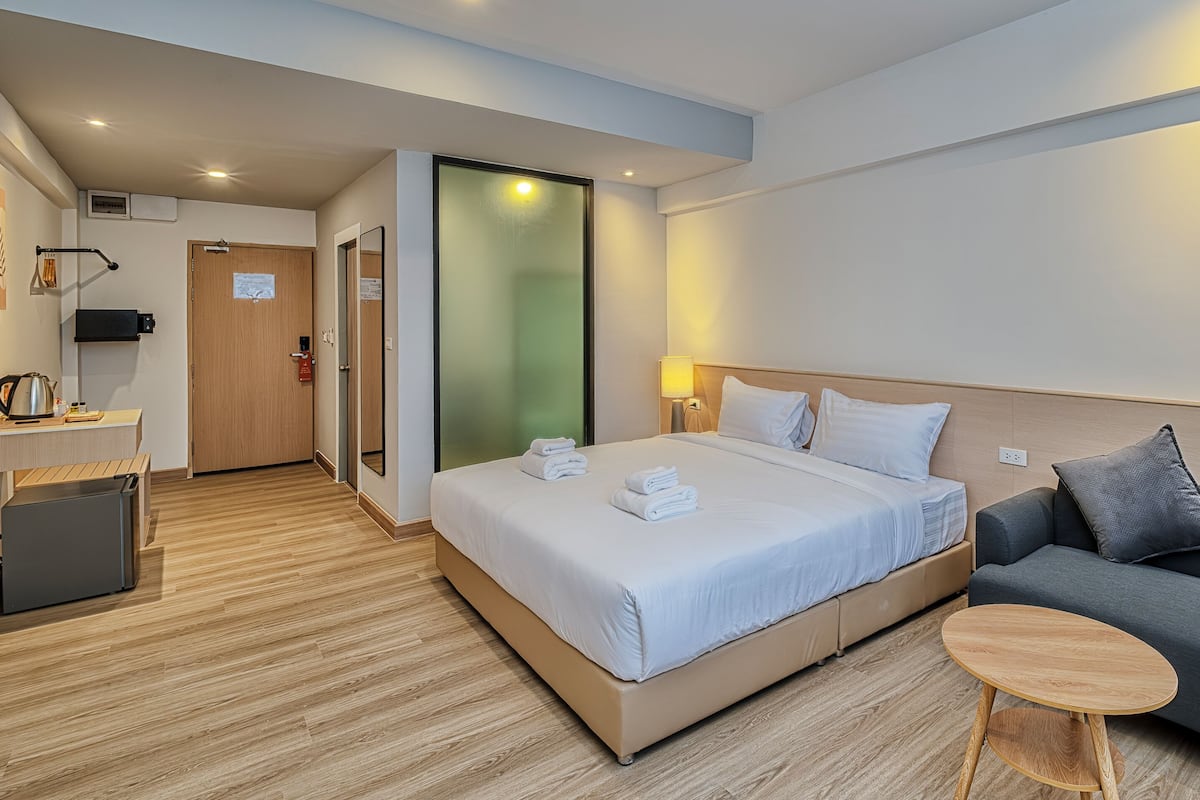 A hotel room with a bed, a sofa, a small table, a desk with a computer, and a microwave.