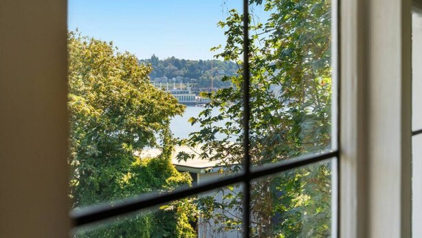 Vista por una ventana que muestra un cuerpo de agua, árboles y una costa distante.